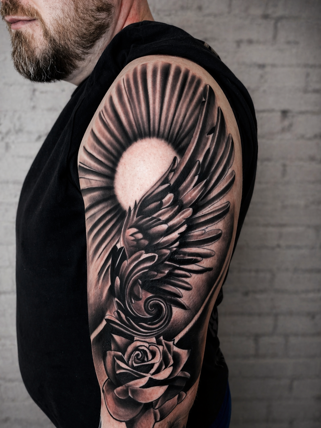 Black and grey wing and rose upper arm tattoo by Rondon Neto