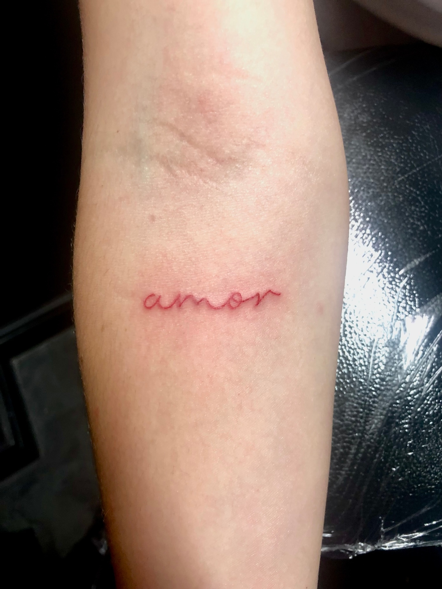 Fine line red ink 'amor' script tattoo by Rondon Neto